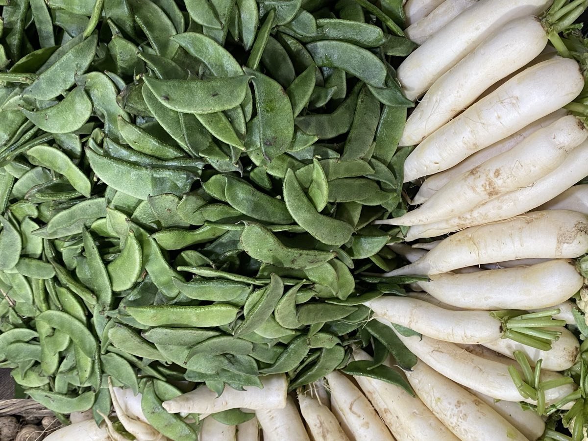 Fresh green beans and white radishes stacked at a market stall